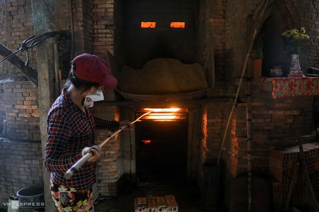 Chị Kim Loan (40 tuổi, chủ l&ograve; gạch) th&ecirc;m trấu v&agrave;o l&ograve; nung gạch. Chị cho biết, mỗi l&ograve; chứa khoảng 15.000 vi&ecirc;n, nung trong 20 ng&agrave;y th&igrave; ra th&agrave;nh phẩm."Nh&agrave; t&ocirc;i c&oacute; hai l&ograve; gạch, đỏ lửa hơn 20 năm nay. C&ocirc;ng việc n&agrave;y kh&ocirc;ng c&ograve;n mang lại thu nhập cao như trước nữa n&ecirc;n giờ chỉ l&agrave;m r&aacute;ng giữ nghề, c&ograve;n con c&aacute;i th&igrave; cho theo ng&agrave;nh kh&aacute;c th&ocirc;i", chị Loan chia sẻ.